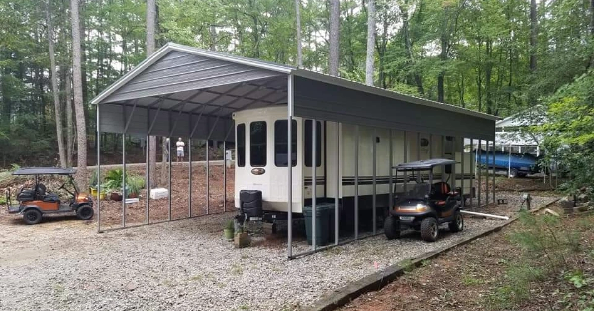 A carport structure being used to protect a RV in a wooded landscape.
